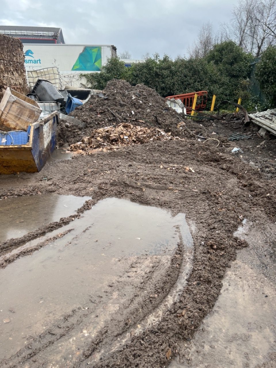 Wolverhampton yard covered in rotted cardboard and mud with a skip and stacked bales