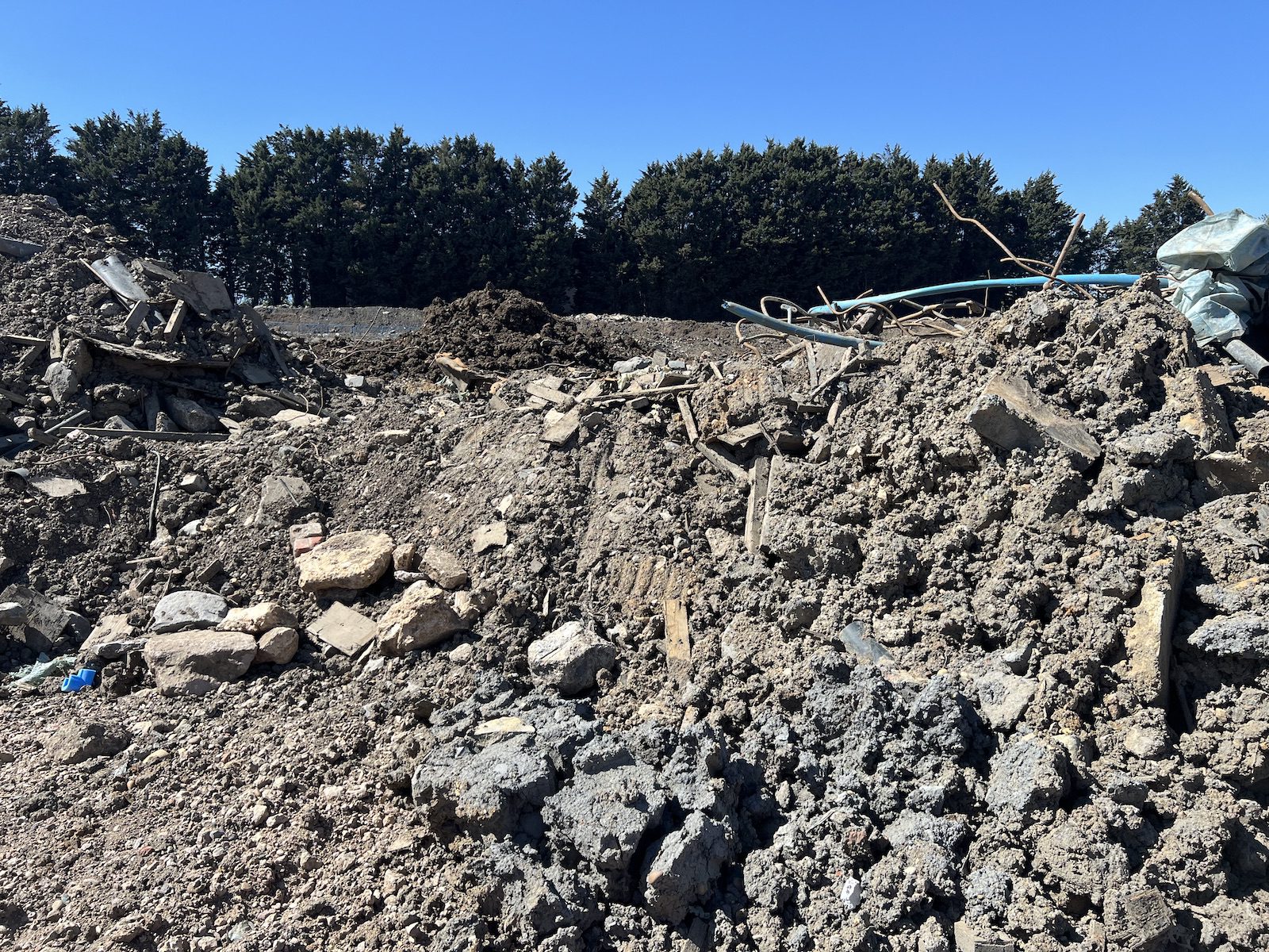Mixed spoil of soil, broken concrete, timber and old pipework awaiting classification
